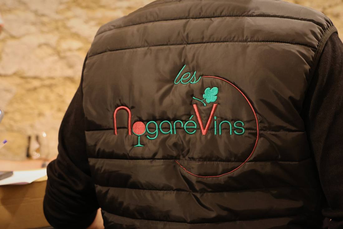 Le logo de l'association Les Nogarévins brodé dans le dos d'une doudoune sans manches, devant un mur de pierre