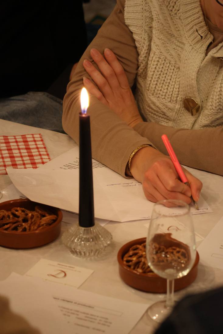 Une main prend des notes sur une fiche de dégustation, à côté d'une bougie et d'un verre
