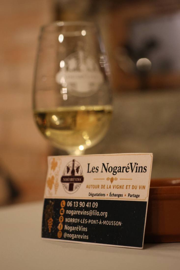 Un verre de vin blanc et la carte de l'association Les Nogarévins posée sur la table, pendant leur cours d'œnologie à Norroy-lès-Pont-à-Mousson