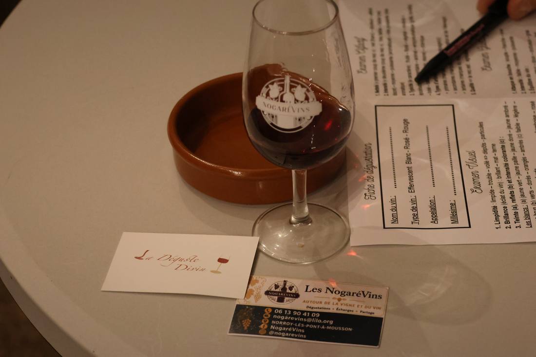Un verre de vin rouge, une fiche de dégustation et une carte de visite sur une table ronde