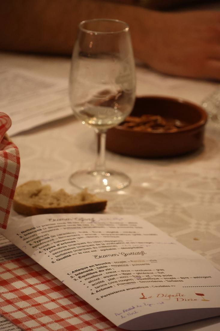 Un verre de vin blanc, une fiche de dégustation et du pain sur une serviette à carreaux rouges