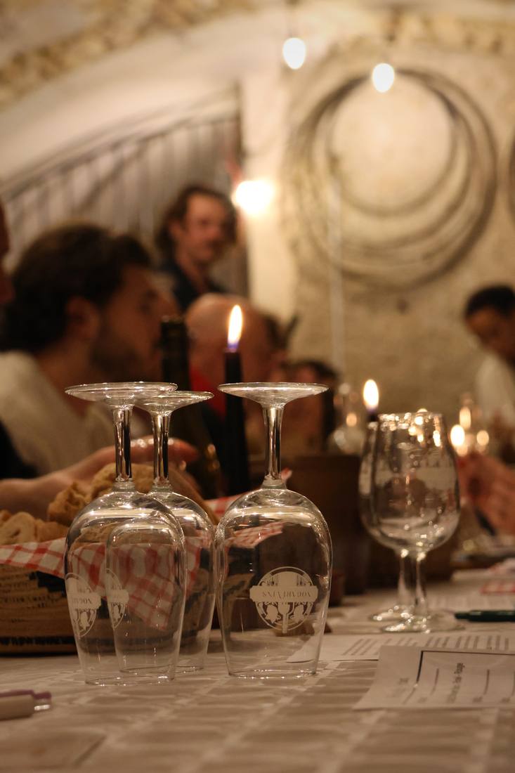 Verres à dégustation et bougies allumées sur une table nappée de blanc, pendant le cours d'œnologie des Nogarévins, dans une cave voûtée