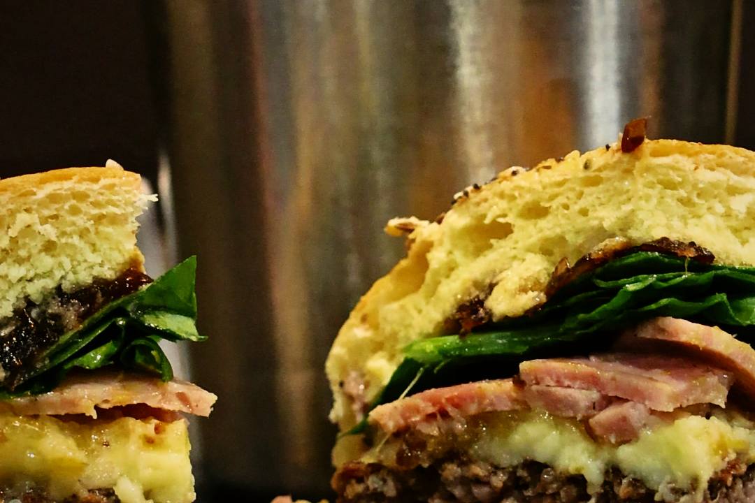 Un burger coupé en deux, fromage fondu et pousses d'épinard, devant un pot de frites maison chez Vache Burger, à Nancy