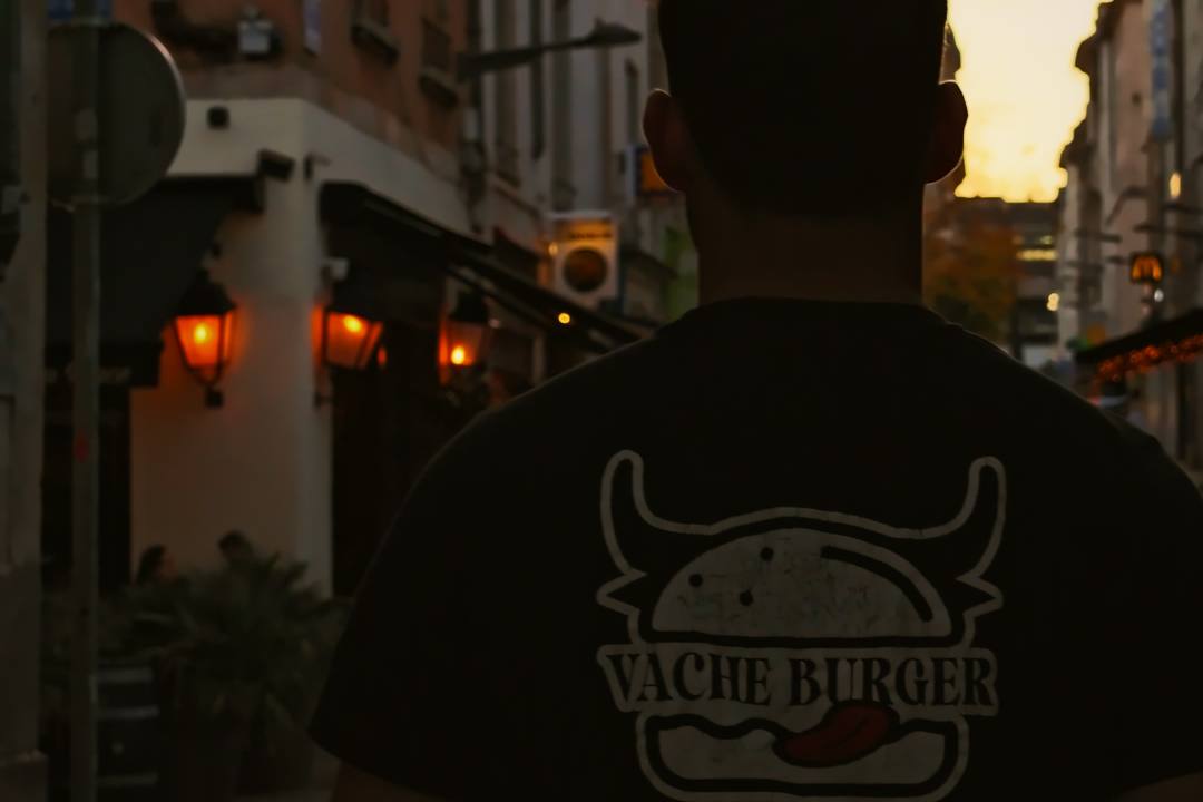 Un membre de l'équipe de dos, en tee-shirt Vache Burger, dans une rue de Nancy à la tombée du jour
