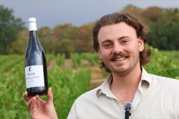 Une bouteille tenue à la main devant la vigne