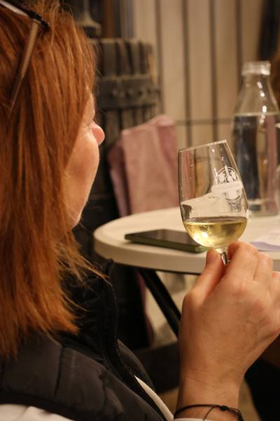 Une dégustatrice de dos, son verre de vin blanc à la main
