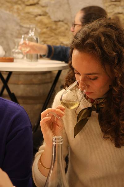 Une dégustatrice sent un verre de vin blanc, dans une cave aux murs de pierre