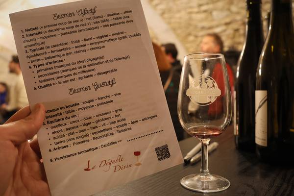 Une fiche de dégustation tenue à la main, à côté d'un verre de vin rouge