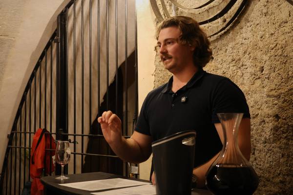 Maxence présente un vin devant une grille de cave